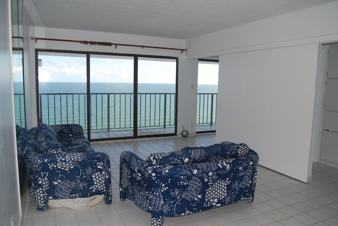 Photo of living room with couch and loveseat with Gulf views through the windows at By The Sea Condominiums